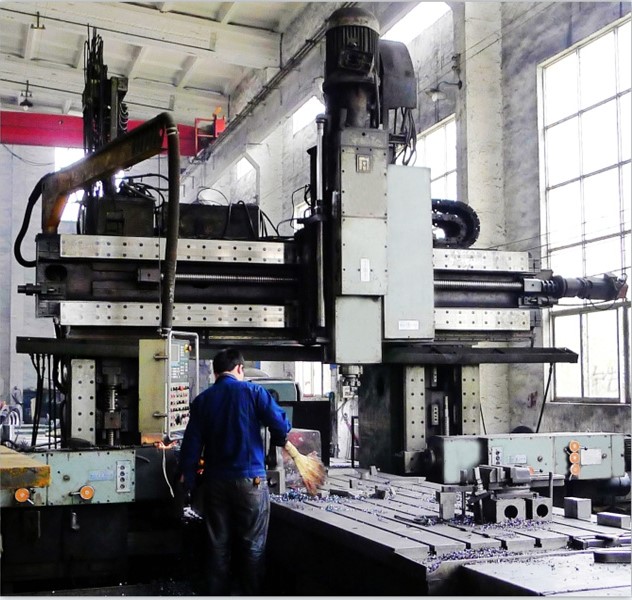 A large-scale CNC gantry milling machine with a 2m x 6m worktable, shown machining a large steel workpiece in a modern factory setting.