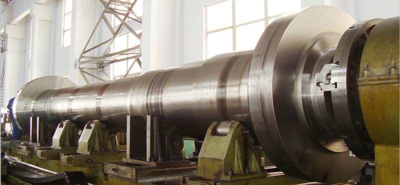 A large motor shaft being precision-turned on a heavy-duty CNC lathe in a modern manufacturing workshop.
