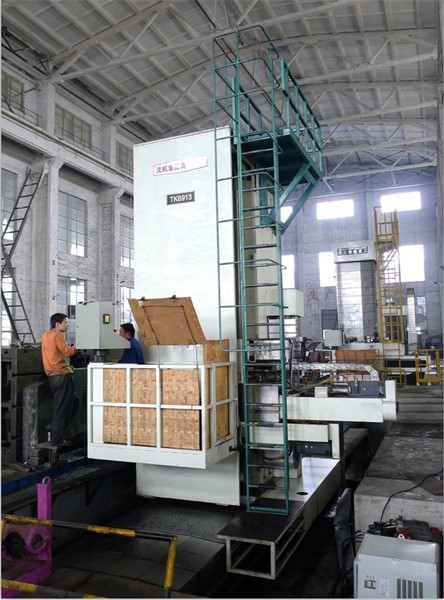 The large TK6913 CNC floor-type boring and milling machine in a factory, shown processing a large, complex workpiece on its floor plate.